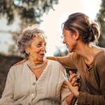 Elderly woman and adult daughter share a joyful, affectionate moment in a sunny garden.