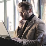 Man looking contemplative while working on a laptop in a well-lit indoor space.
